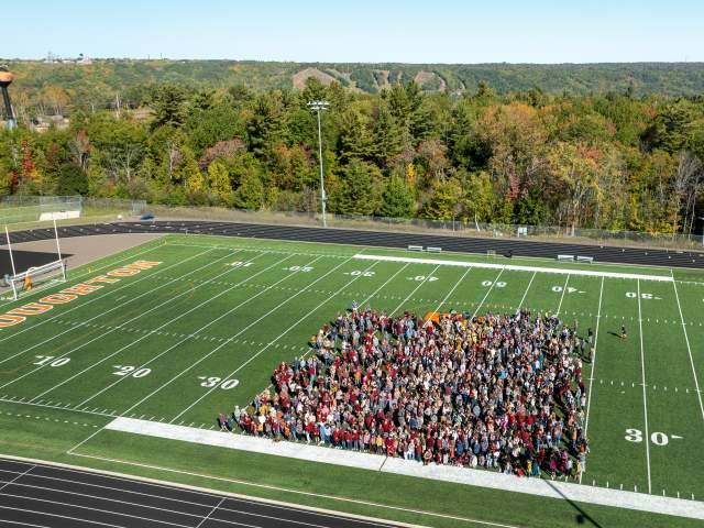 aerial view of over a thousand people standing in a square on a football field