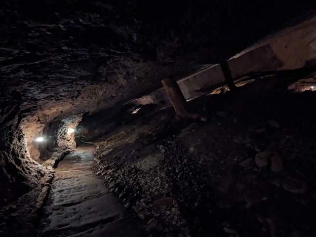 lantern light illuminates into a long pathway underground, the light softly outlining features of the excavated mine shaft