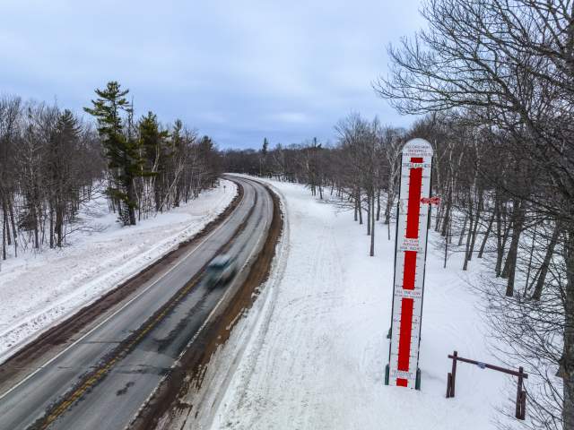 a tall thermometer marking annual snowfall stands tall in the snow along a highway