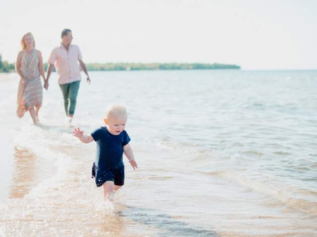 Parents trail behind a toddler on Lake Superior shoreline.