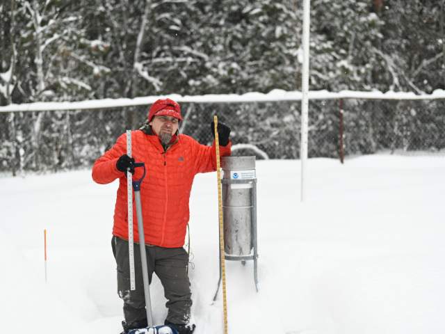 a person stands next to a NOAA snowfall measurement tool in deep snow