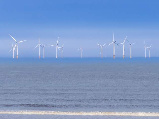 Offshore windfarms on the Lincolnshire Coast with a beach in the foreground under blue skies