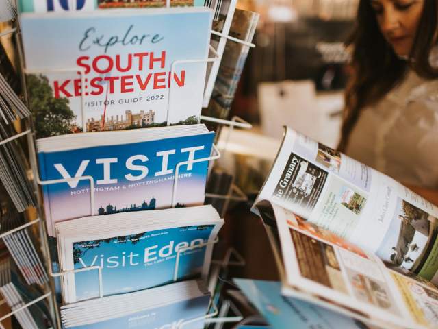 a stand with brochures and books about tourism with a woman at the left reading a leaflet