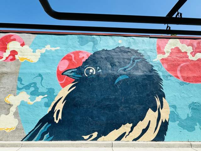 Mural of a magpie with clouds and red circles on a blue background on a wall