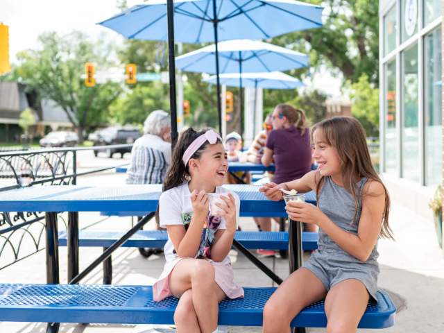 patio with benches, umbrellas, and two young girls eating iced cream