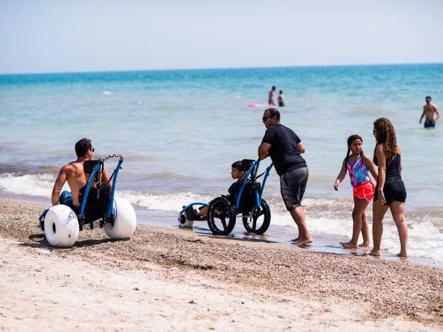 People use beach wheelchairs to enjoy the Lake Michigan on a sunny day