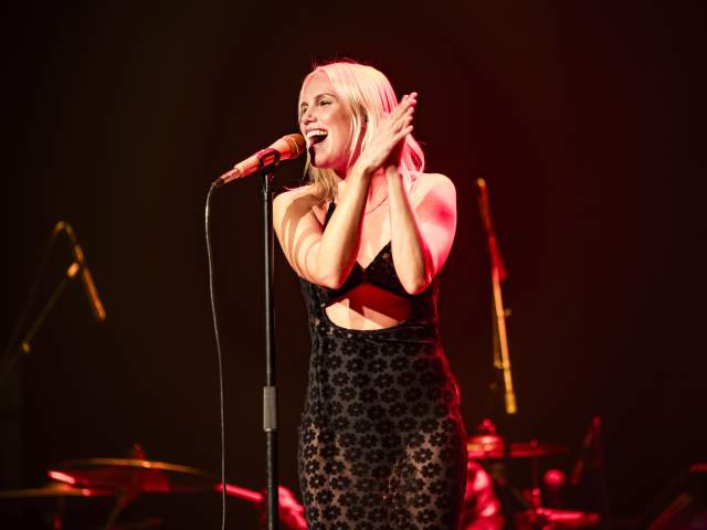 Grace Weber smiling as she sings into a standing microphone and claps