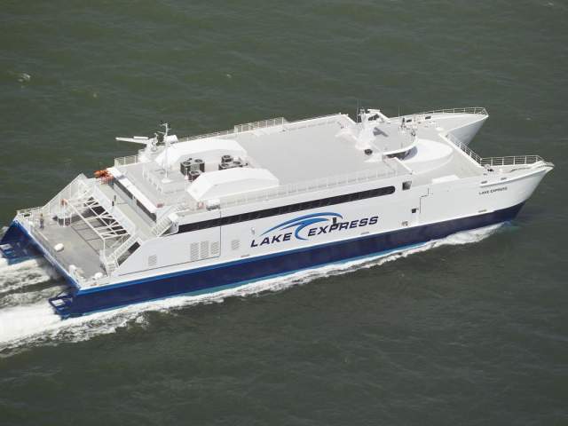 Aerial view of the Lake Express high-speed ferry traveling across Lake Michigan, showing its white and blue exterior with the logo 'Lake Express' on the side.