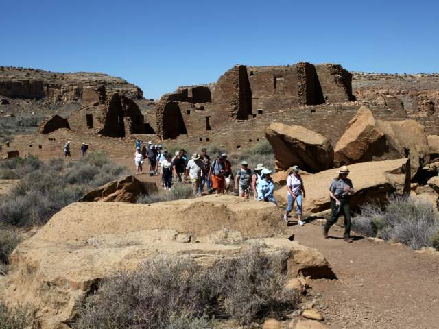 A Group Of People Walking Single File Through Chaco Canyon