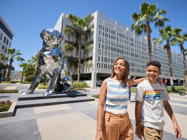 Boy and girl pose in front of mirror dog sculpture in Lake Nona
