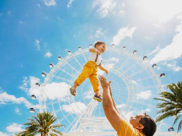 father throwing son up in air in front of The Wheel at ICON Park