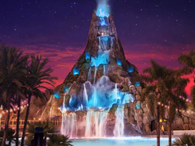A towering volcano glows over the lagoon at night at Universal Volcano Bay Nights
