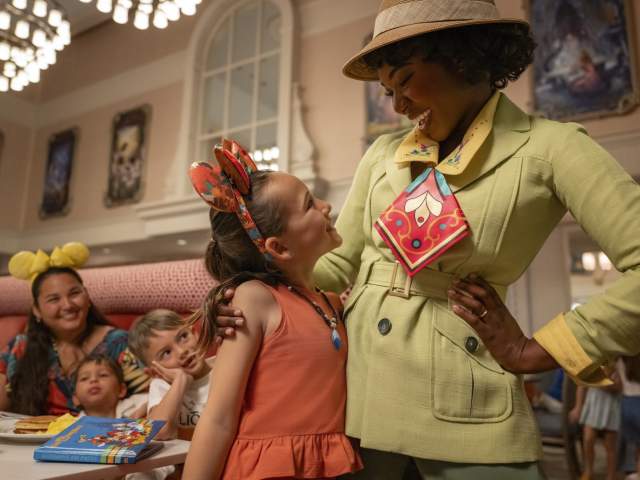 A little girl smiles up at Tiana during a character dining breakfast at 1900 Park Fare at Walt Disney World Resort