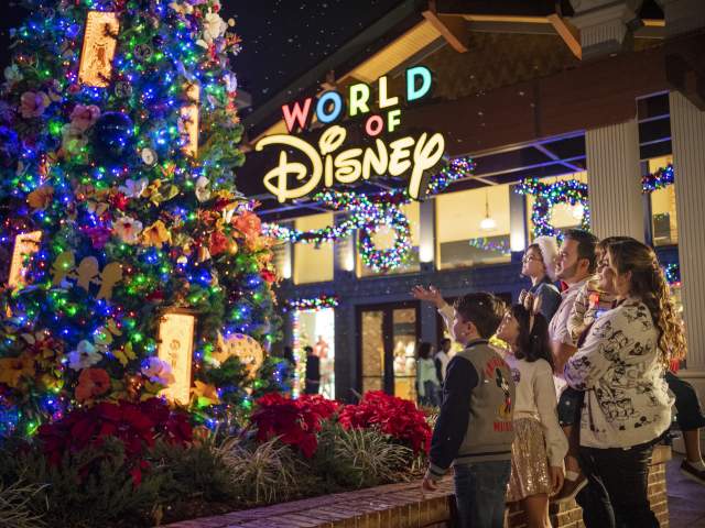 A family admires a vibrant Encanto Christmas tree outside World of Disney as part of the Christmas Tree Stroll at Disney Springs