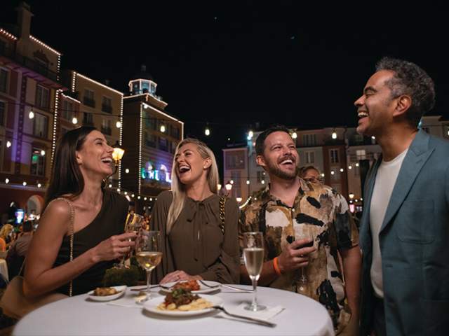 Four adults laughing as they gather over evening wine and small plates at Loews Portofino Bay Hotel