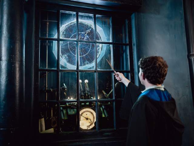 A teen points an interactive wand at a window display in the Wizarding World of Harry Potter, activating a celestial dial