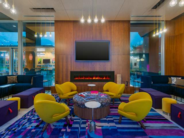 Sleek Aloft Orlando hotel lobby with vibrant purple carpet, four yellow chairs and a modern in-wall fireplace