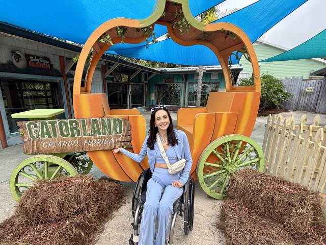 Accesibility influencer Amanda Perla poses in her wheelchair in front of a large pumpkin carriage at Gatorland Orlando