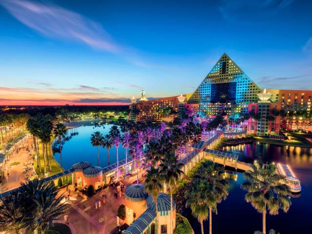 The Walt Disney World Swan and the causeway connecting to the Walt Disney World Dolphin, all lit up in dazzling yellow, blue and purple lighting for the evening