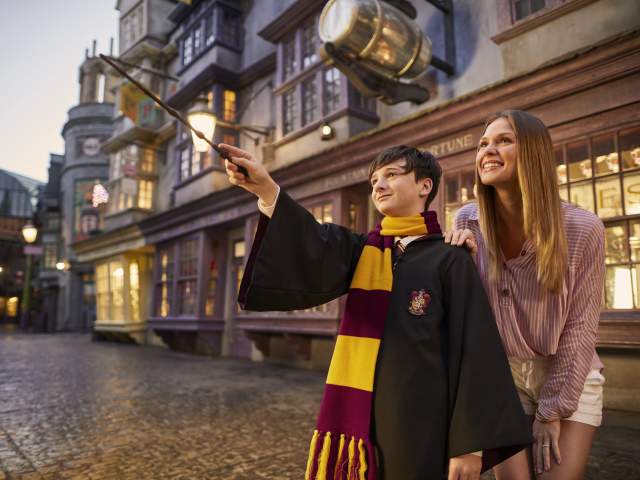 boy dressed as Harry potter waves wand while mom watches