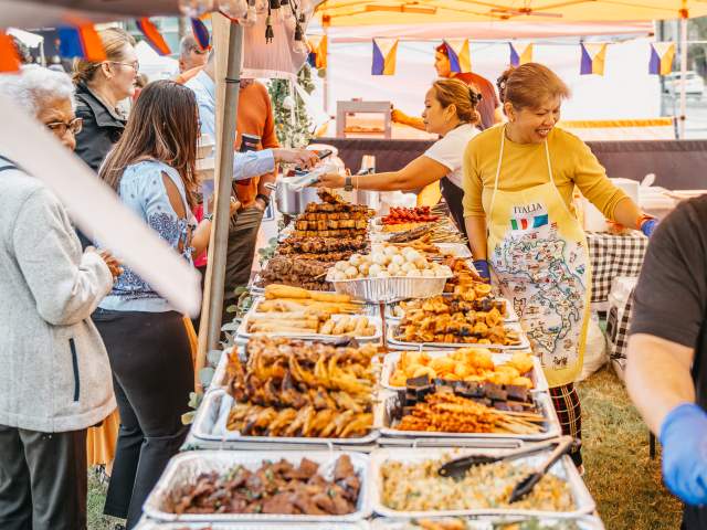 A woman smiles as she serves visitors from catering trays packed wih exotic food options