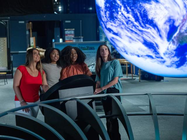 Four young women gaze in wonder at a floating model of the planet Earth inside the Orlando Science Center