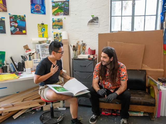 Two men chatting in an art-covered artists studio at the Art & History Museums of Maitland