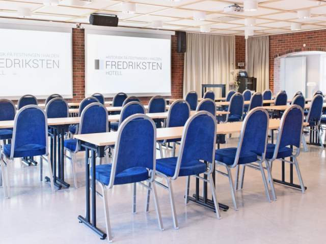 Konferanserom med blå stoler og skjermer