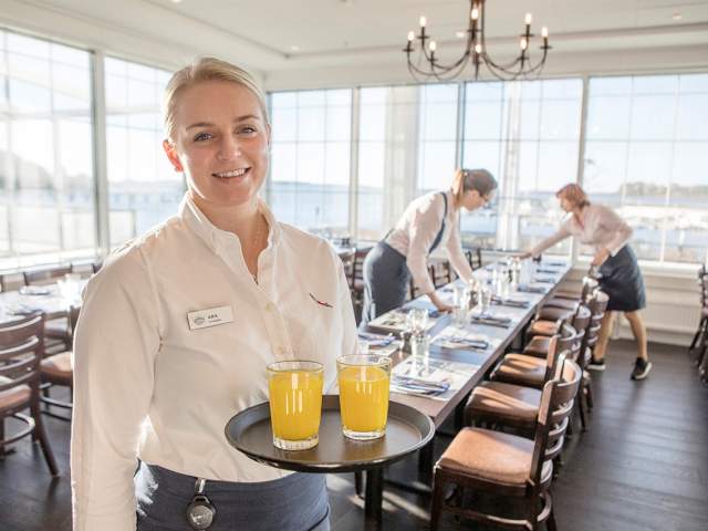 Kvinnelig servitør smiler mot kamera med et serveringsbrett i hånden