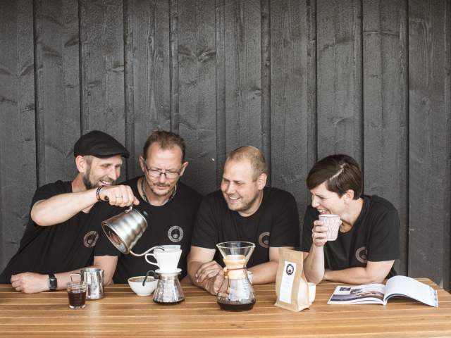 Tre menn og en kvinne koser seg med kaffe på Ørje Kaffebrenneri