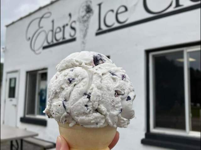 A hand holding up a waffle cone of ice cream in front of a sign that reads Eder's Ice Cre