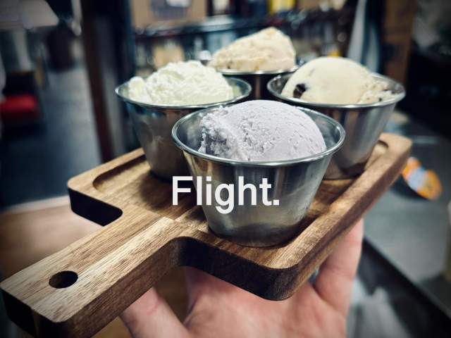 A hand holding up a wood serving platter with four small cups on it filled with ice cream. The text overlay reads Flight.