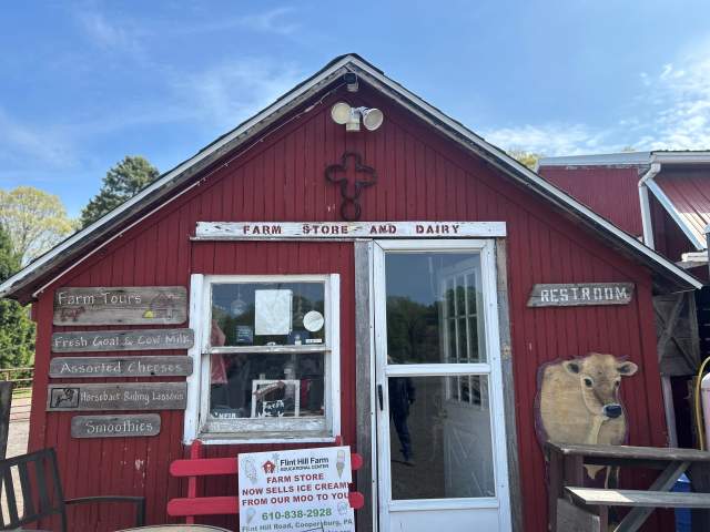 Exterior of a red, ice cream shack with a sign above the screen door that reads Farm Store and Dairy