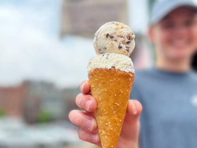 A woman in a ball cap holding up an ice cream cone with signage in the background