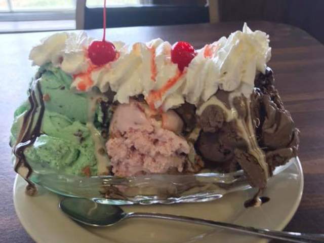 A large ice cream sundae with mint, strawberry, and chocolate ice cream with whipped cream and a cherry on top