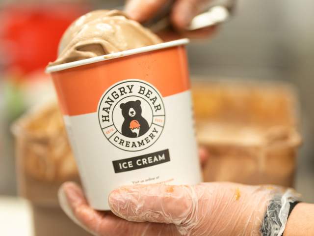 A person scooping ice cream into a paper cup with the Hangry Bear Creamery logo