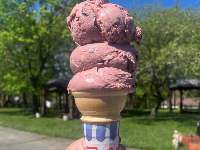 A hand holding an ice cream cone with three scoops of purple ice cream