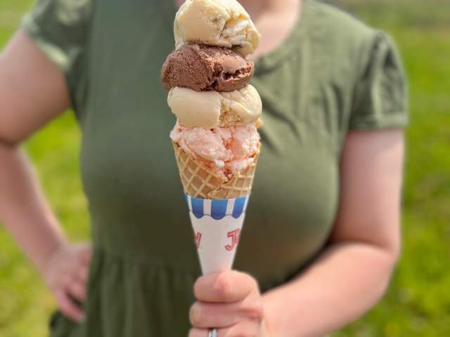 Person holding up an ice cream cone with three scoops of ice cream