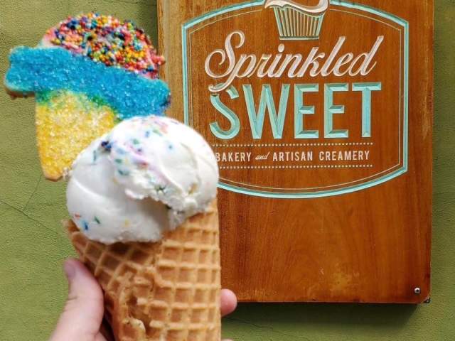 An ice cream cone in front of a sign that reads Sprinkled Sweet