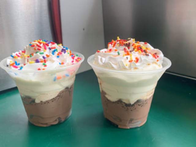 Two clear plastic cups both filled with vanilla and chocolate ice cream with sprinkles on top
