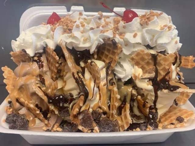A takeout container with waffles cover in ice cream, chocolate sauce, and whipped cream