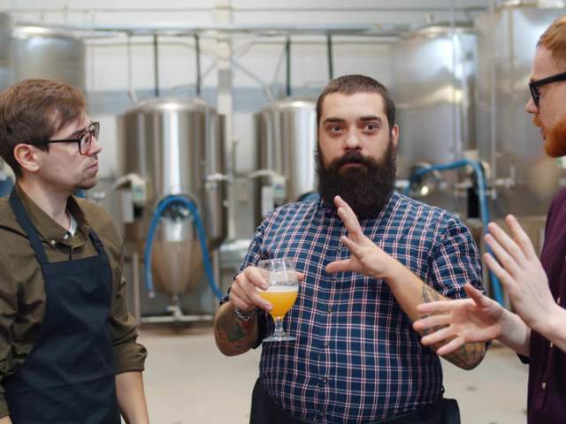 Man holding a pint of beer while talking with two other men on a brewery