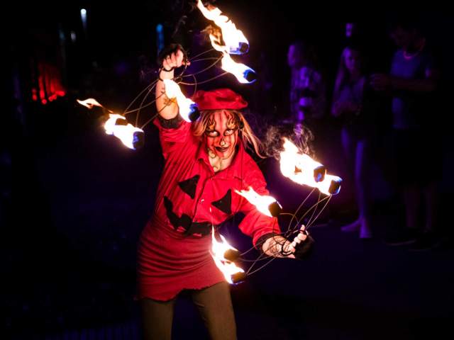 A person in costume juggling torches of fire in the dark at Eastern State Penitentiary.