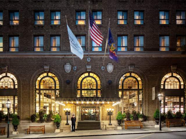 An exterior of a historic hotel with three flags hanging off the entrance at night