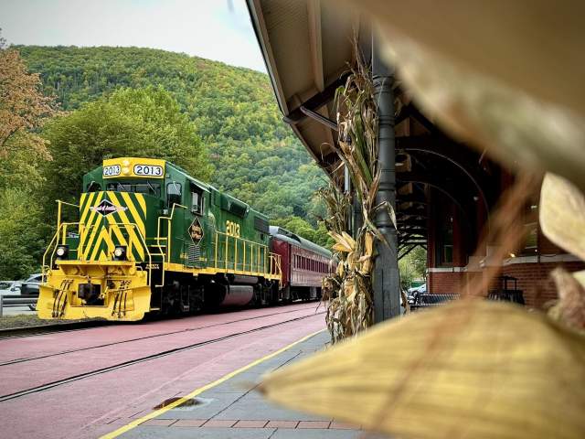 A bench at a train station with a parked green and yellow locomotive train