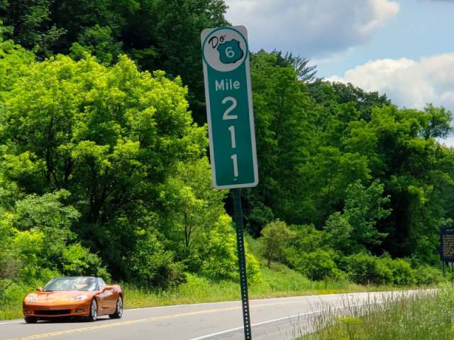 A car driving on an open road with a mile marker that reads 211
