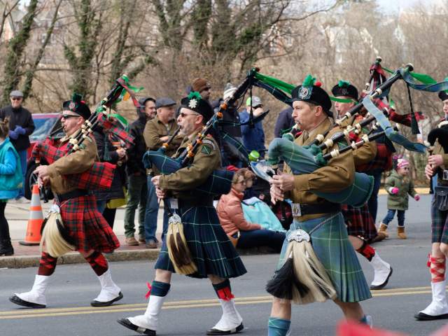 A group of men dressed in traditional Irish attire and kilts playing bag pipes in a street parade