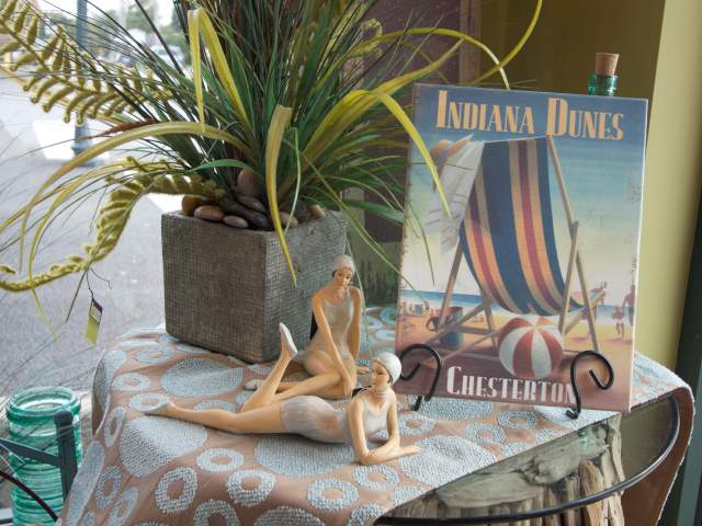 An sign, plant, and two statues site on a display table. The sign says "Indiana Dunes Chesterton" and the statues are ladies in old fashioned swimsuits.
