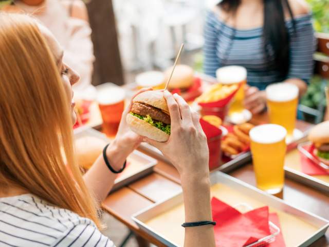 A red-haired woman is eating a burger outside at a table with other people.