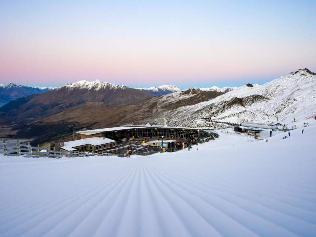 View of ski resort from top of a snowy mountain with snow capped mountains in background